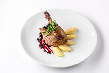 Duck leg baked with apples and currant sauce on white plate close-up view from above.