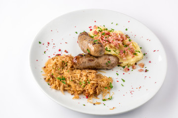 Grilled sausages, potatoes and braised cabbage on white plate close-up view from above.