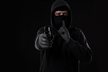 Masked robber with gun aiming into the camera against a black background