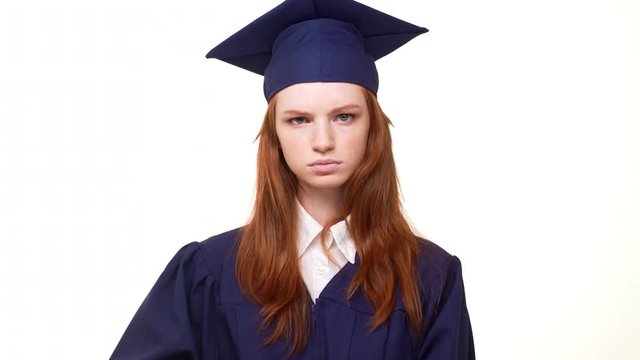 Foxy Caucasian beautiful graduate girl in academical dress putting finger to lips calling to silence. Footage on white background