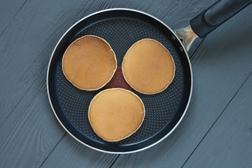 Three pancakes in a frying pan on wooden surface