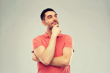 man in polo t-shirt thinking over gray background