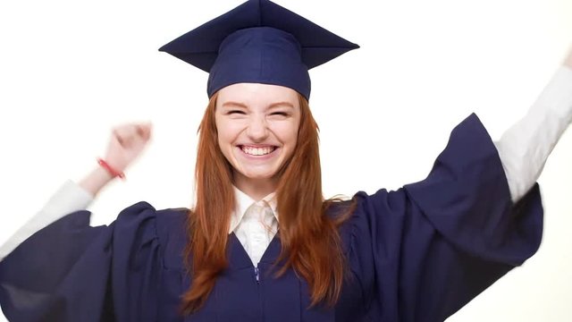 Young happy graduate Caucasian girl with gignger hair rejoicing on white background in slowmotion