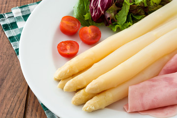 White asparagus with salad and ham on wooden background

