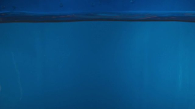 Closeup of a lemon falling into water on the blue background slow motion