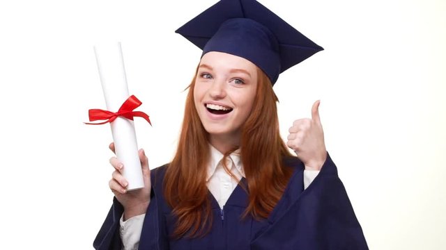 Exciting Caucasian ginger graduate girl in blue robe and square academical cap showing diploma scroll and rejoicing in white background in slowmotion