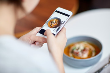 woman with smartphone photographing food at cafe
