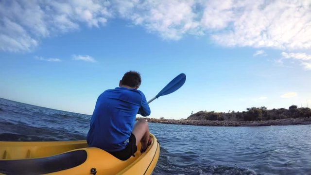 Active and dynamic POV shot from water of a fit healthy strong man in blue active wear paddling a yellow adventure kayak to the safety of shore, on holiday summer destination