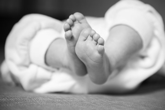 Little infant baby boy sleeping laying, feets up, in focus. Neutral black background, black and white picture. In white clothes. Happy family