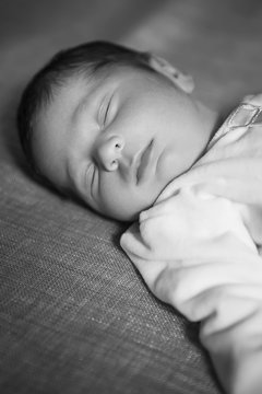 Little infant baby boy sleeping laying on bed, in focus. Neutral black background, black and white picture. In white clothes. Happy family