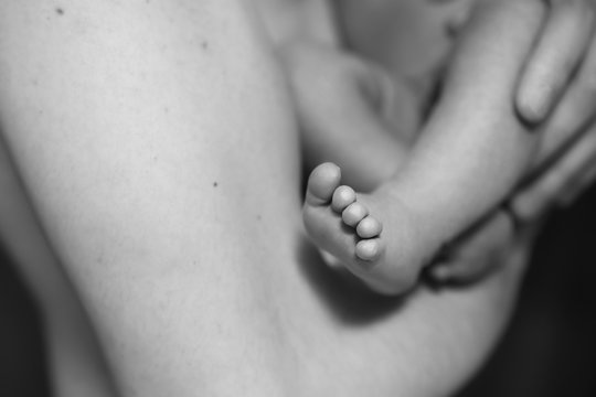 Little infant baby boy sleeping laying on fathers arms. Focus on a boy feet. Neutral black background, black and white picture. All naked. Happy family