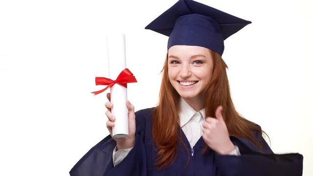 Happy smiling foxy young graduate girl in blue academical dress entering frame holding her diploma. Footage on white background in slowmotion