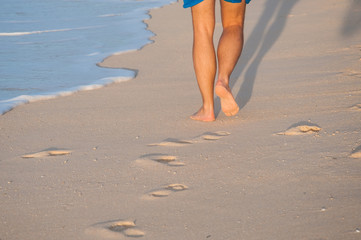 Closeup of a man's bare feet walking at a beach at sunset, with a wave's