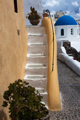 Typical Greek architecture on Santorini Island, Greece. Yellow painted staircase in the foreground and white Church with blue dome in the background.