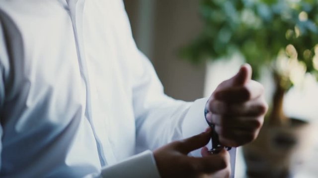 Man in a white shirt puts on a watch. Young businessman getting ready at the morning. Close-up view of male hands.