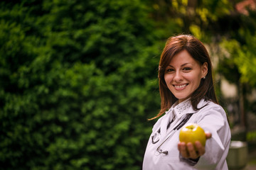 Portrait of a beautiful smiling female doctor offering you an apple