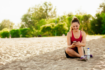 Fototapeta na wymiar Beautiful woman sitting on sand beach and holding phone