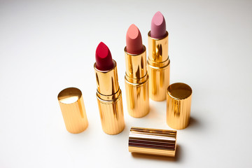 Three open lipsticks of red, pink and beige colors on a white background. Near open caps from lipsticks