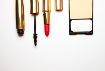 Red open lipstick, black mascara for eyes, compact powder for face and powder brush on white background. view from above. Fashionable women's cosmetics