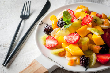 Vegan dietary food. Vitamins Summer dessert. Salad of fresh organic fruits mango, peach, apple, banana, kiwi, strawberry, blackberries. On white marble plate, white concrete table copy space