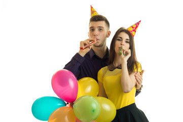 Fototapeta na wymiar funny young couple celebrating birthday with cones on their heads keep colored balls and blow horns