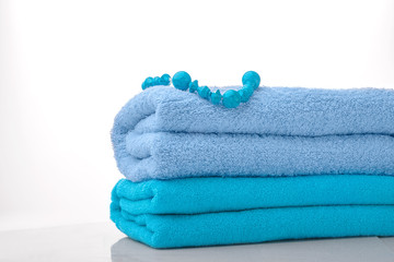 Two Terry towels and beads on a white background. Blue towels are already on the stack, and beads of turquoise. The Studio photos. High key. The concept of purity freshness SPA
