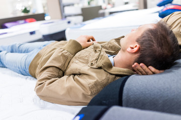 Young man trying out laying down on mattress on display in store