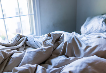 Messy bed sheets in dark blue room closeup with window