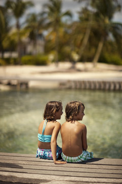 Two happy young children relaxing on a wooden pier on their tropical island holiday.