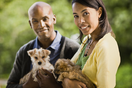 Young heterosexual couple smile as they hold puppies and pose for a portrait.