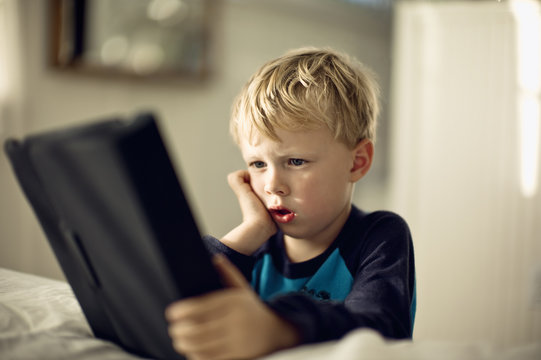 Young boy looking serious as he plays with a portable information device.
