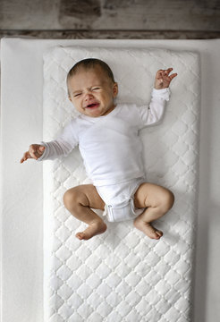 Overhead view of baby girl crying while lying on bed