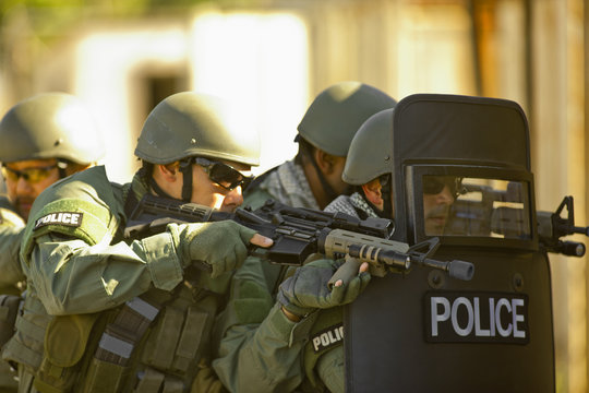 Four police officers holding weapons and  protection about to enter a building during an exercise at a training facility.