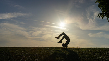 Male contortionist doing a scorpion yoga pose at sunset