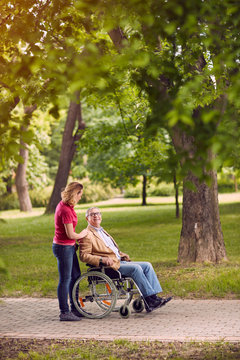 elderly man in wheelchair talking with daughter in the park.