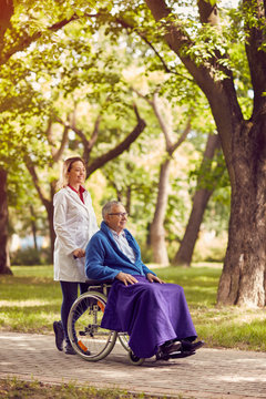 senior man in wheelchair with nurse in the park.