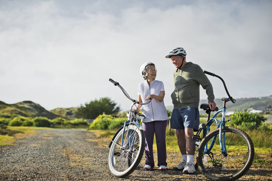 Happy elderly couple chat together as they take a break from biking along a country road.