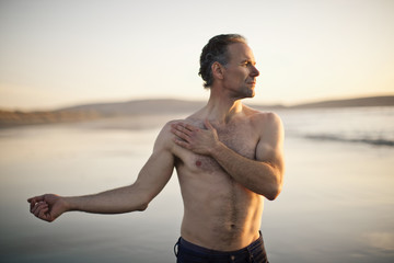 Shirtless man stretching on the beach.