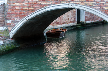 Fototapeta na wymiar Boat under a bridge in Venetian Canal, Venice, Italy
