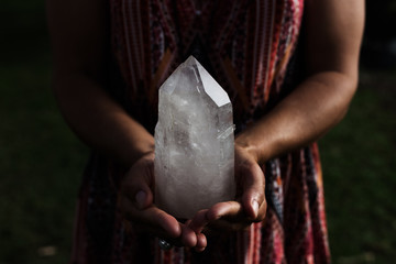 A young woman holding a large, luminous quartz crystal appears powerful in dramatic lighting. - obrazy, fototapety, plakaty