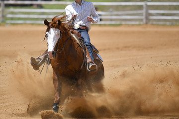 The front view of a rider in cowboy chaps and boots sliding the horse in the sand