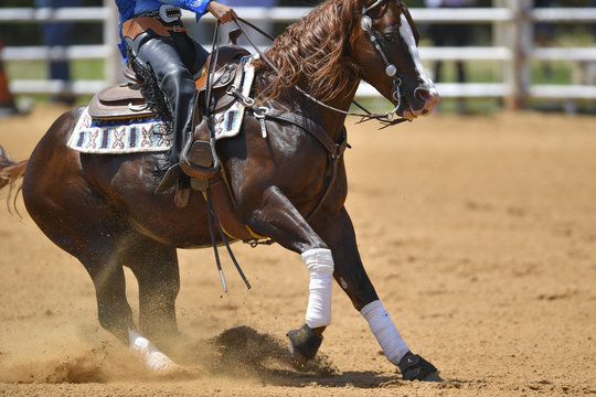 A side view of a rider sliding the horse in the dirt
