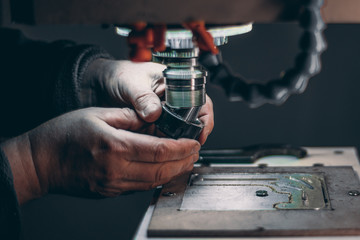 View of worker hands while he is changing drilling tool cutter in CNC milling machine during pause of treatment of aluminum blank fixed on moving table in dark settings of workshop room © skyNext