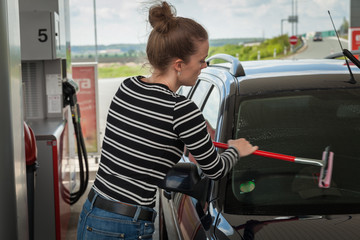 Young woman washing the glass of a car at a petrol station