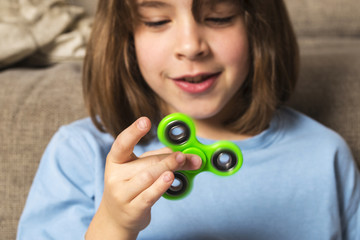 Little girl playing with green fidget spinner toy - obrazy, fototapety, plakaty