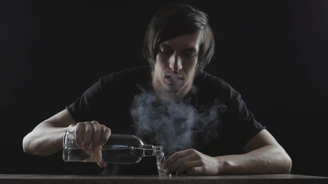 Close up of man drinking vodka alone in a dark room in slow-motion