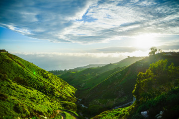 Small valley leading to the sea with green hills and a blue cloudy sky