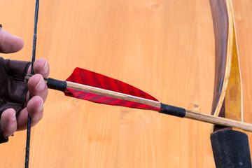 Archer wearing open fingers leather gloves drawing a traditional english longbow with a red feather...