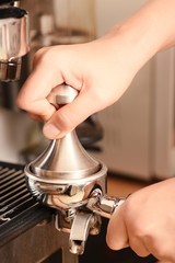 Barista holding tamper to press ground coffee in a portafilter for making coffee from espresso machine