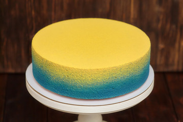 Blue and yellow cake on stand over wooden background